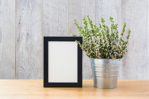 White picture frame and plants in can on wooden desk