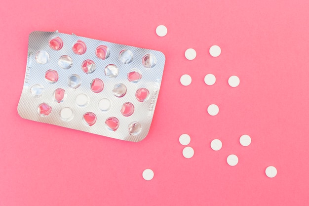 White pills and blister pack on pink background