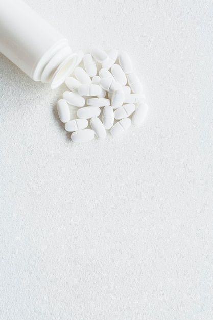 White pills and plastic bottle on white background