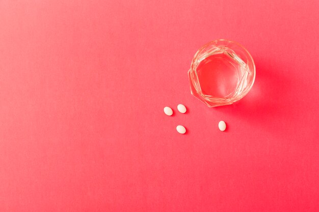 White pills with glass of water over the red background