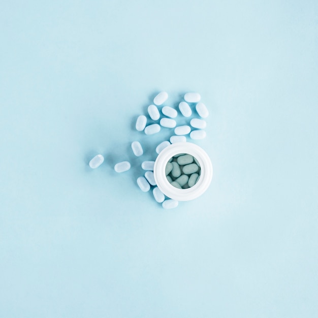 White pills with open plastic bottle on blue background