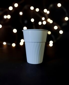 White plastic cup in dark room with lights background