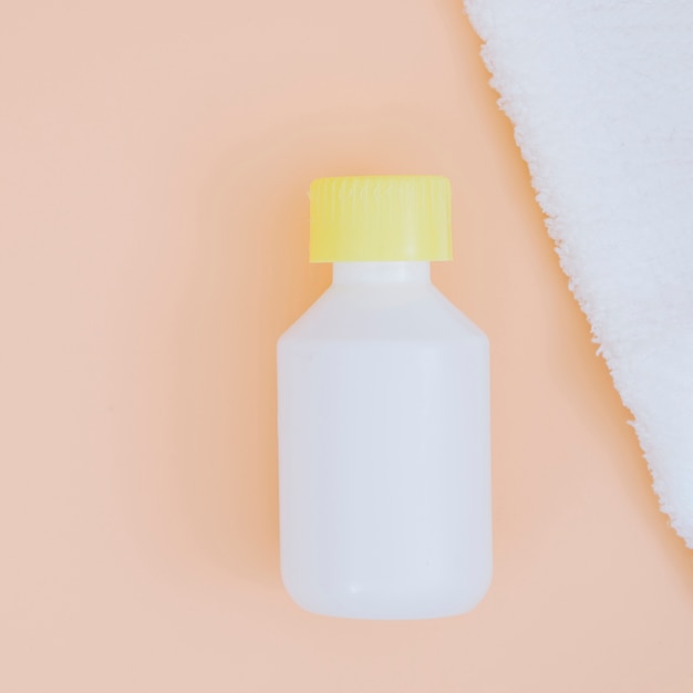 White plastic detergent bottle with yellow lid on peach backdrop with white napkin