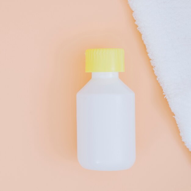 白いナプキンと桃の背景に黄色いふた付きの白いプラスチック製洗剤ボトル