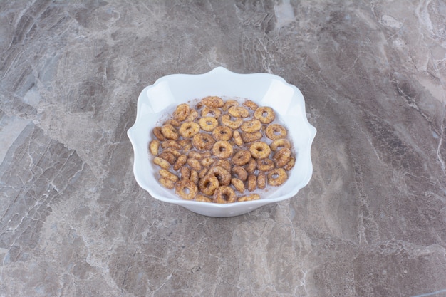 A white plate of chocolate cereal rings with milk on gray table. 