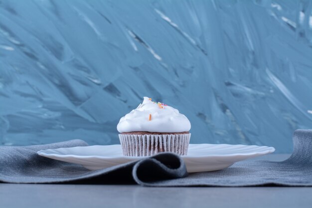 A white plate of a creamy cupcake with colorful sprinkles . 