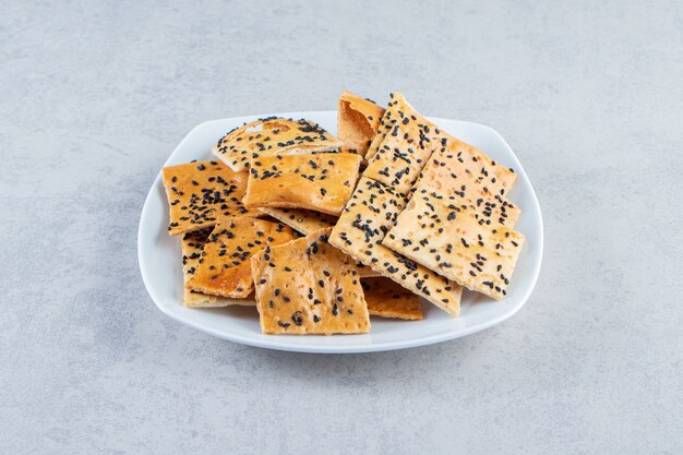 White plate of crispy crackers with black seeds on marble background.