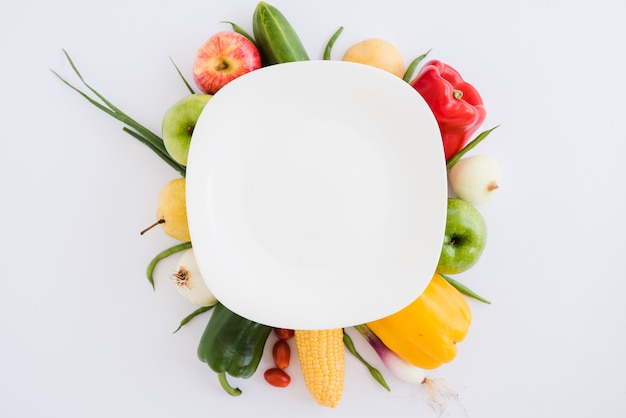 White plate over the cucumber; apple; bell pepper; onion; corn and scallions on white backdrop