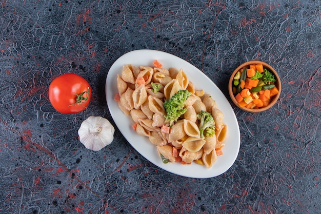 White plate of delicious seashell pasta and fresh salad on marble surface. 