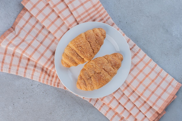 A white plate of delicious sweet croissants on striped tablecloth.