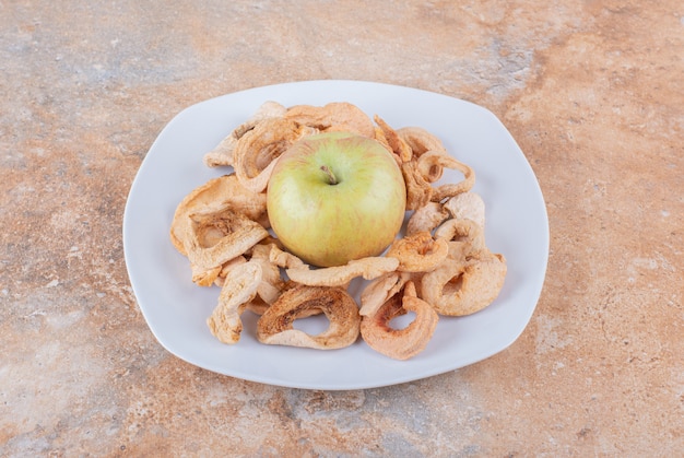 White plate of dry apple rings and fresh green apple on marble table. High quality photo