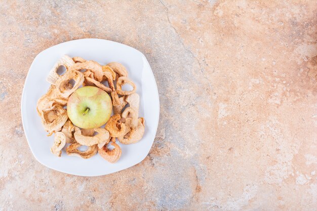 White plate of dry apple rings and fresh green apple on marble table. High quality photo