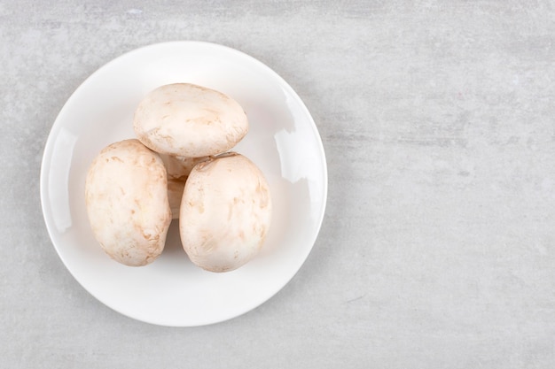 White plate of fresh big mushrooms on stone table.