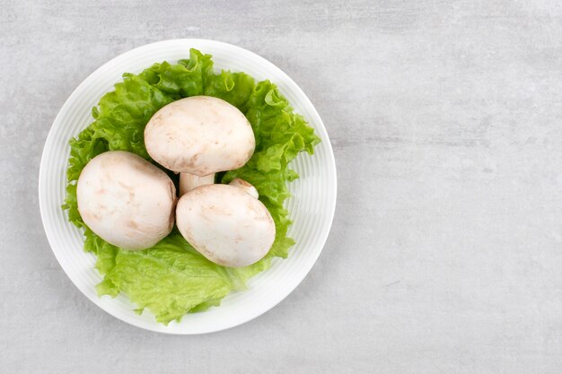 White plate of fresh white mushrooms and lettuce on stone table. 