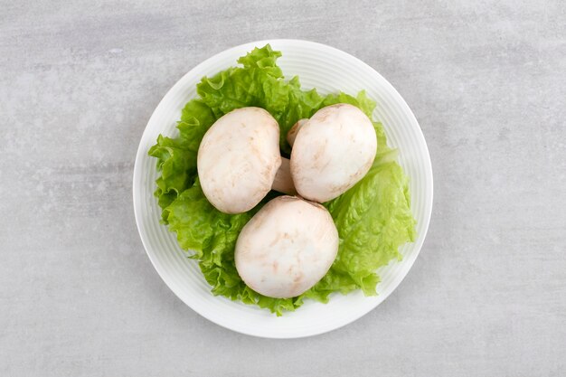 White plate of fresh white mushrooms and lettuce on stone table. 