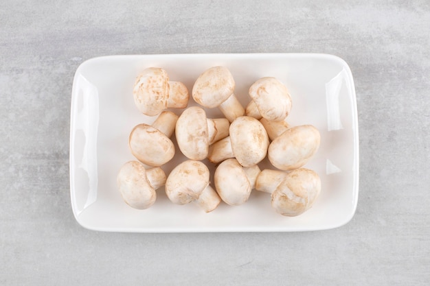 White plate of fresh white mushrooms on stone table. 