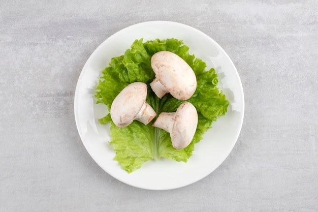 White plate of fresh white mushrooms on stone table. 