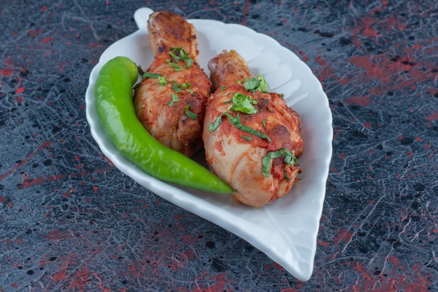 A white plate of fried chicken legs with chili pepper.