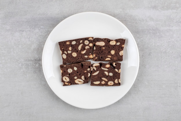 Free photo white plate full of brown bread slices with nuts on a stone surface.