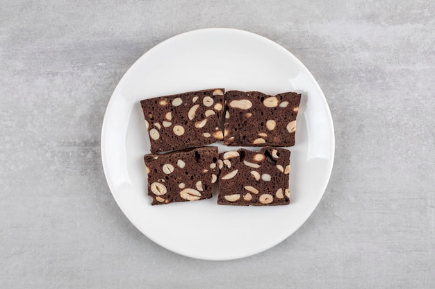 White plate full of brown bread slices with nuts on a stone surface.
