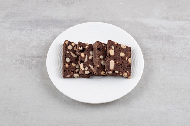 White plate full of brown bread slices with nuts on a stone surface.