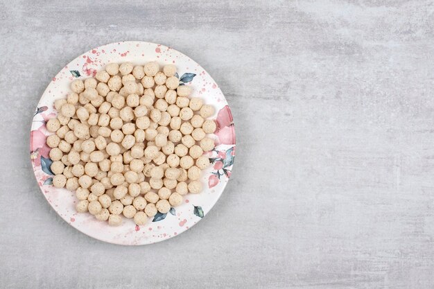 Белая тарелка, полная шариков кукурузных хлопьев на каменном столе.