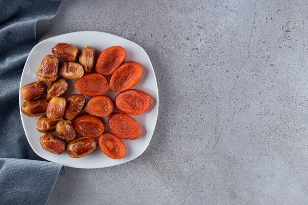 White plate full of dried dates and apricots on stone surface