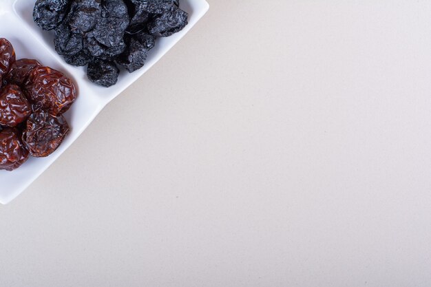 Белая тарелка, полная сушеных вкусных слив на белом фоне. Фото высокого качества