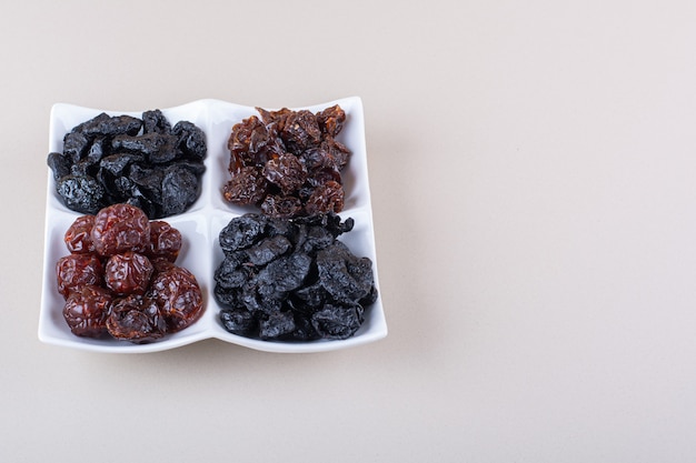 White plate full of dried tasty plums on white background. High quality photo