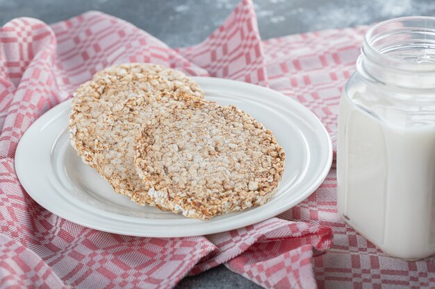 A white plate full of puffed rice bread with a jar of milk .