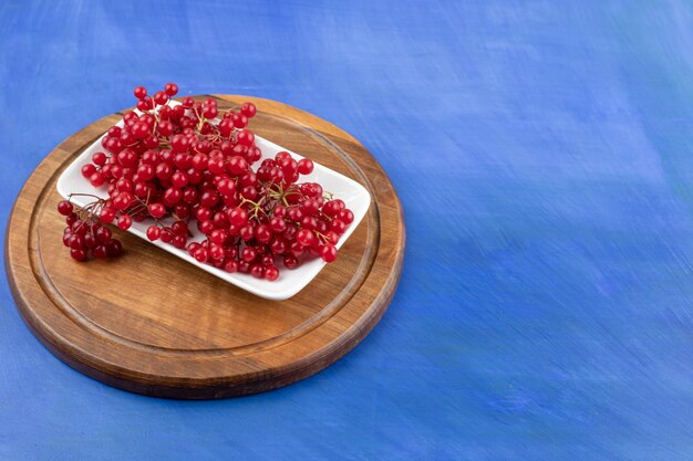 A white plate full of red currant on blue surface