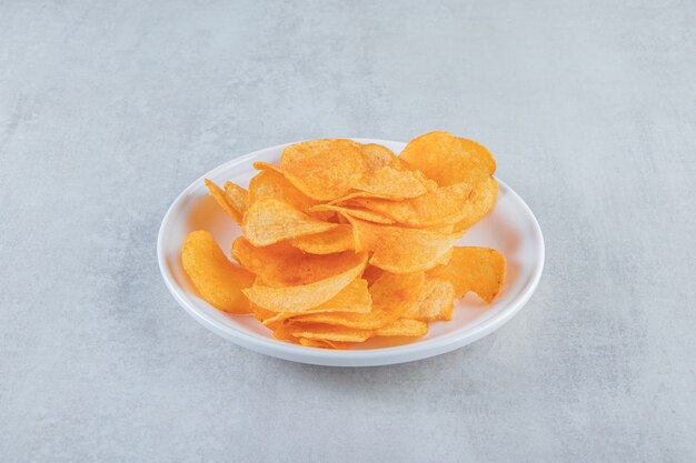 White plate full of spicy chips placed on stone.