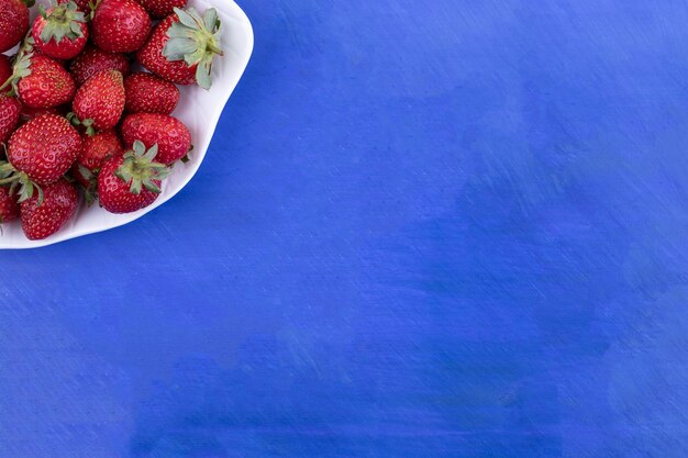A white plate full of strawberries on blue surface