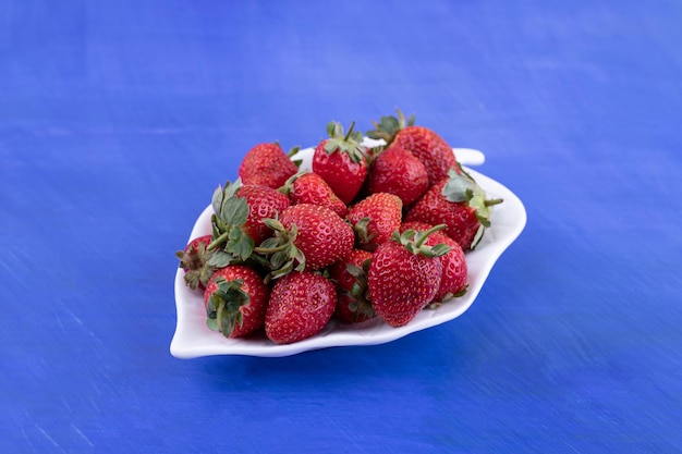 A white plate full of strawberries on blue surface