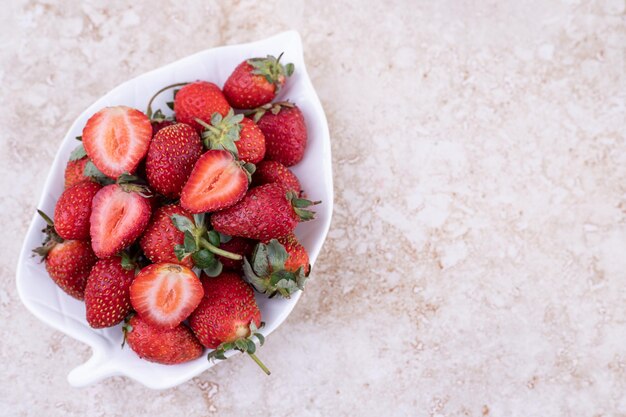 A white plate full of strawberries on marble background.