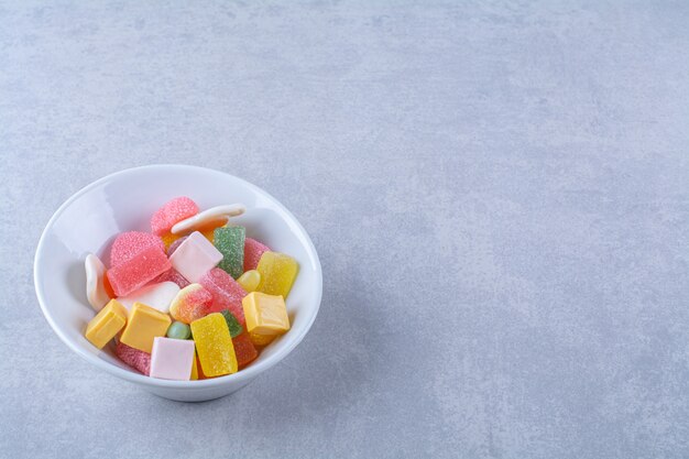 A white plate full of sugary jelly candies on gray surface 