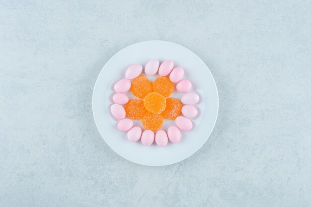 A white plate full of sweet orange jelly sweets and pink candies