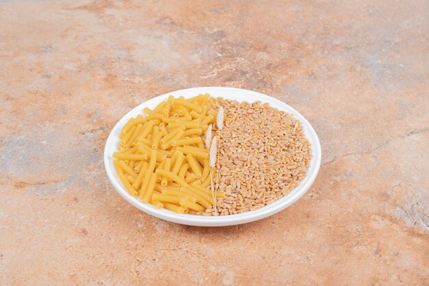 곡물과 대리석 배경에 원시 마카로니와 밀의 흰색 접시. 고품질 사진