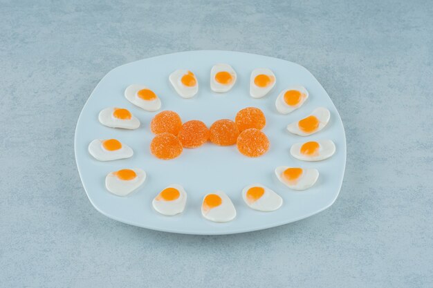 A white plate of orange jelly candies with sugar and marmalade scrambled eggs