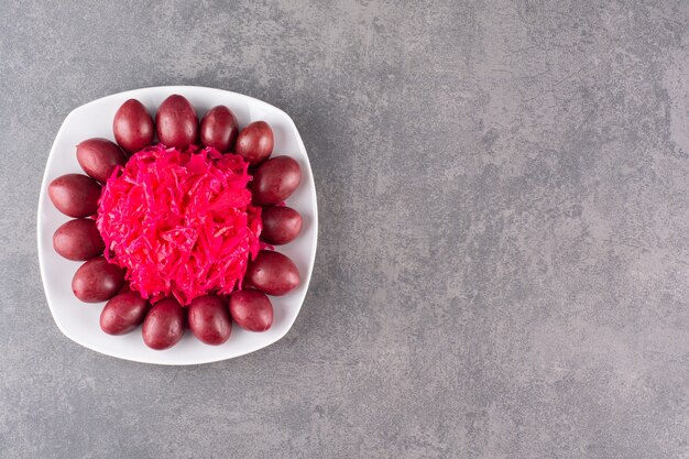 White plate of pickled plums and cabbage on stone table.