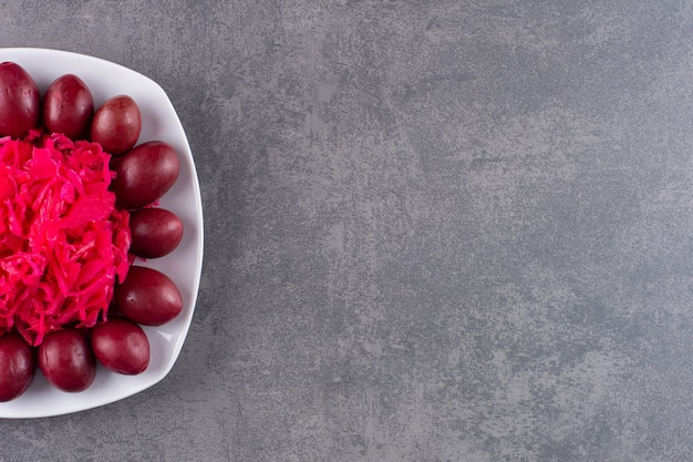 White plate of pickled plums and cabbage on stone table.