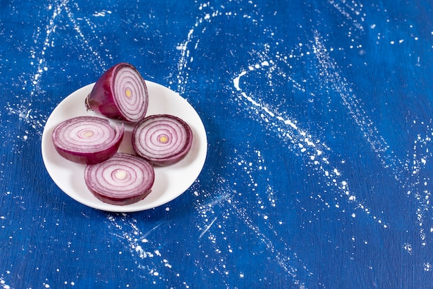 White plate of purple onion rings on marble surface. 