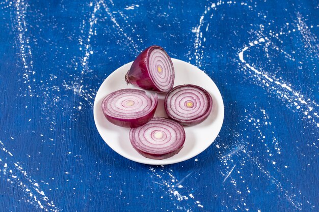 White plate of purple onion rings on marble surface. 