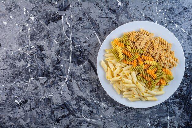 Белая тарелка сырых сухих разноцветных макарон Fusilli с макаронами Penne
