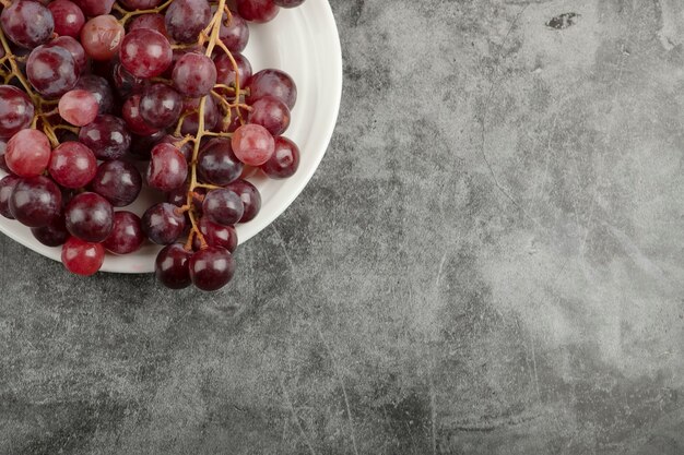 Белая тарелка и красный вкусный виноград на мраморном столе.