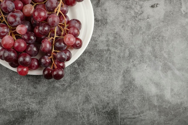 White plate of red delicious grapes on marble table.