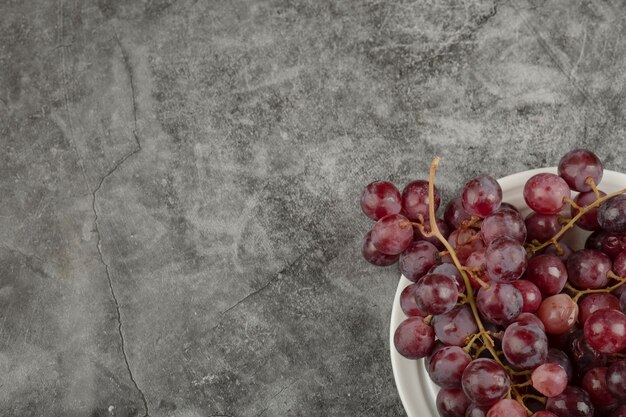 大理石のテーブルに白いプレートとレッドデリシャスのブドウ。