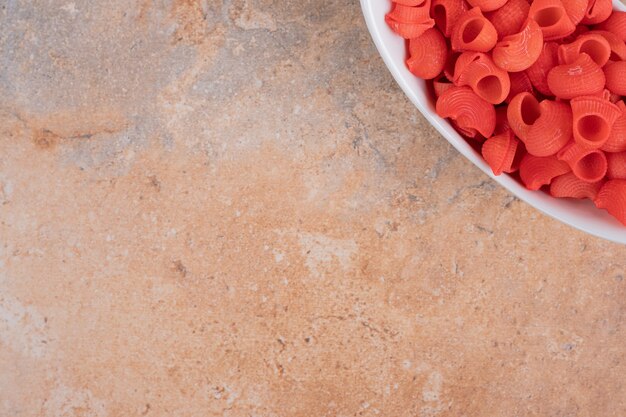 A white plate of red uncooked macaroni on marble background. High quality photo