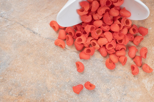 A white plate of red uncooked macaroni on marble space. 