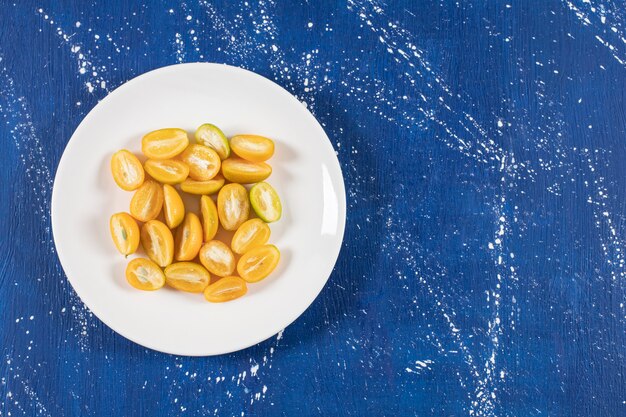 Free photo white plate of sliced fresh kumquat fruits on marble table.